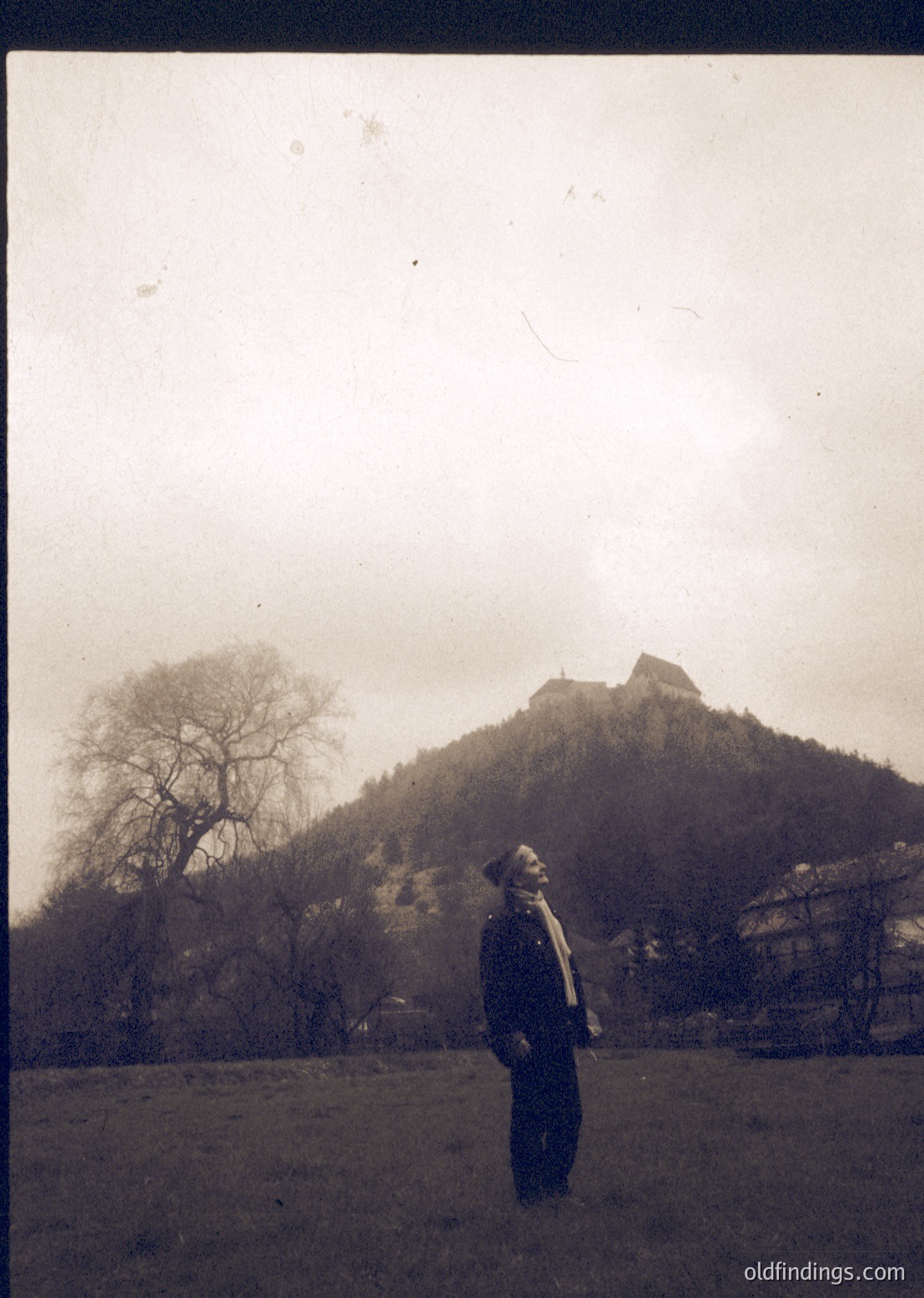 Vintage sepia-toned portrait of a man in early 20th-century attire (wide-brimmed hat, long coat) standing before a rocky hillside with a castle-like structure. Likely Eastern European, possibly or , given architectural style. --- *Note: The exact location is speculative due to lack of identifiable landmarks, but the style aligns with Central/Eastern European castles of the era.*