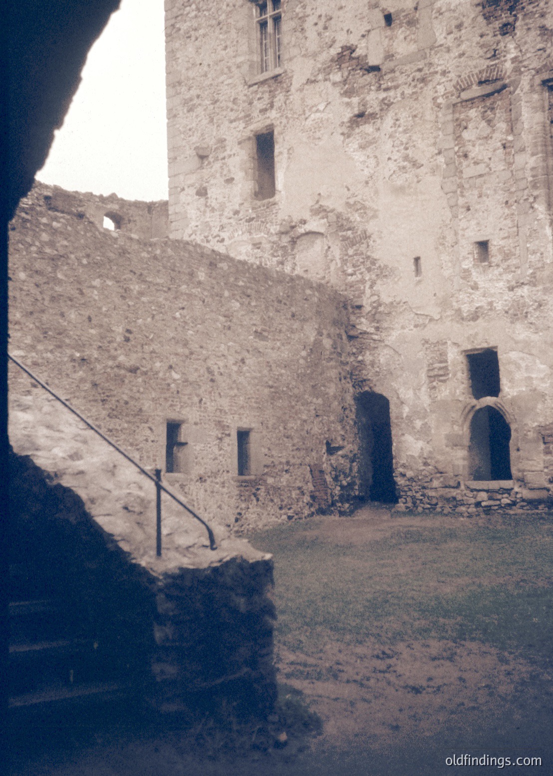 Historic stone courtyard with medieval architecture—weathered walls, arched doorways, and narrow windows. Likely Eastern European fortress or monastery, mid-20th century. Raw, textured surfaces evoke timeless resilience.