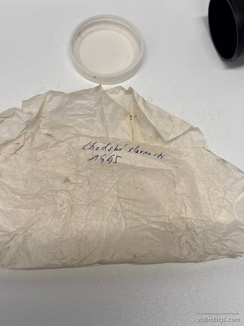 Vintage handwritten label on crumpled paper, dated "1945" with text "Chodzko" (likely a brand or product name). Small metal lid with residue sits atop. Likely a preserved food sample or historical food packaging.
