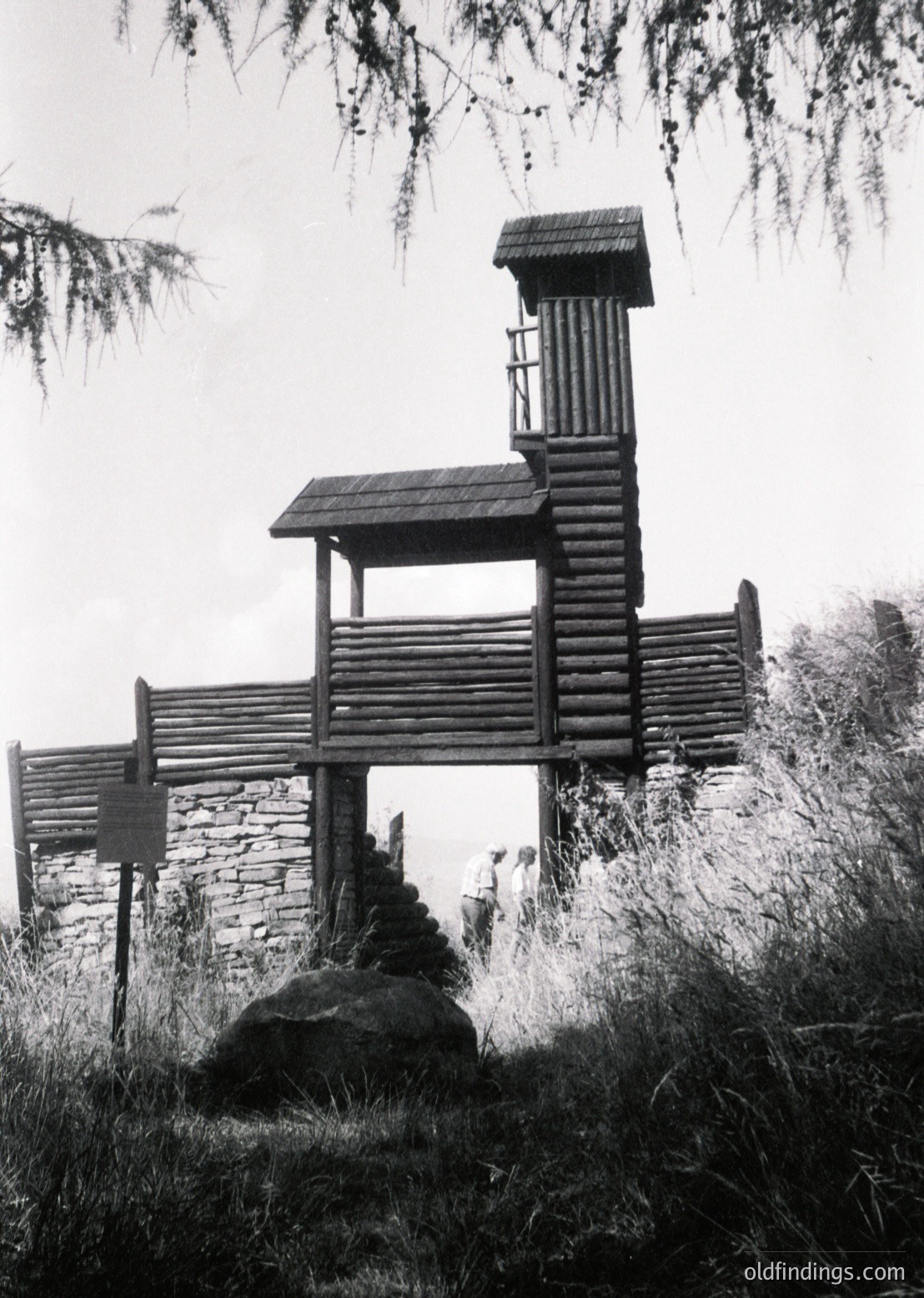 Handcrafted wooden lookout tower with log construction, perched on stone base in forested area. Rustic design features sloped roof and ladder access. Signage suggests restricted or designated area. --- *Note: The time period is inferred from the style and wear of the structure, which aligns with mid-20th-century craftsmanship.*