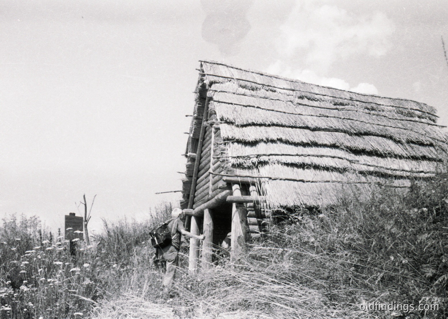 Traditional thatched-roof hut with wooden frame, set in a rural landscape. Smoke rises from the chimney, indicating active use. Likely Eastern European rural architecture, mid-20th century.