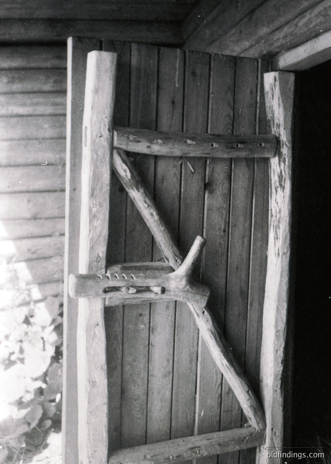 Handcrafted wooden ladder leaning against rustic plank wall, secured by curved metal brackets. Traditional rural architecture, likely Eastern European.
