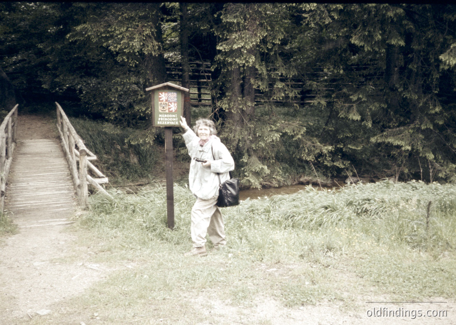 Vintage black-and-white photo of a person posing beside a wooden signpost on a forested trail, likely mid-20th century. The sign reads "Naturreservat" (nature reserve) with a red emblem. Wooden bridge and stone wall visible in background.