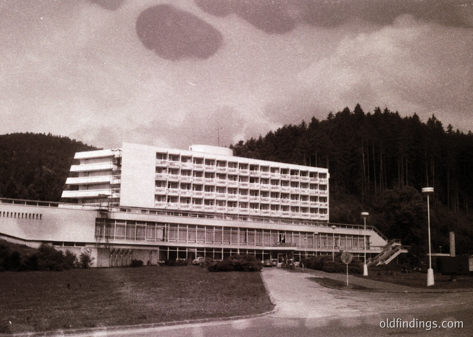 Mid-century Brutalist-style hotel with curved concrete balconies and extensive glass paneling, set against a forested hillside. Likely Eastern European, 1960s-70s era.