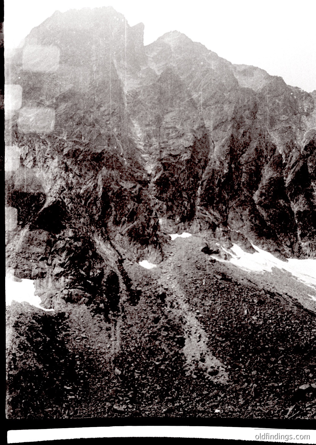 Black-and-white aerial view of rugged alpine terrain with jagged peaks, steep slopes, and scattered snow patches. Likely captured mid-20th century due to monochrome and composition style.