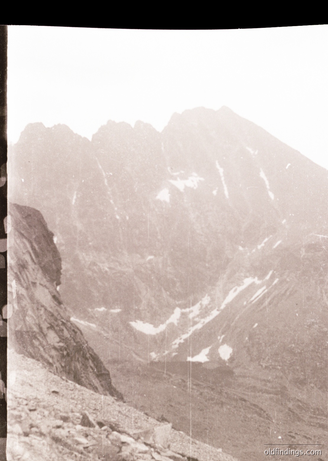 Black-and-white alpine landscape featuring jagged peaks and steep rock formations. Snow patches highlight elevation contrast. Likely captured via vintage slide film () due to framing and grain.