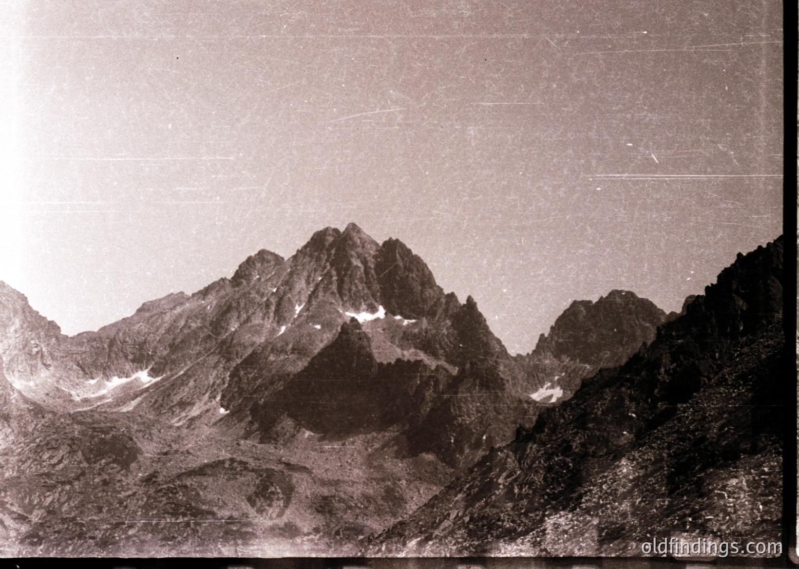 Vintage sepia-toned alpine peak with jagged ridges and snow patches, likely European Alps. Early 20th-century photographic grain and fading edges suggest historical documentation. Dramatic lighting highlights rugged terrain and verticality.