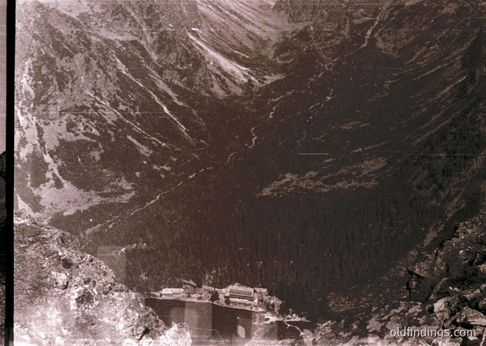 Aerial view of a mountainous region with a prominent dam and reservoir. The dam appears concrete, spanning a valley with forested slopes on either side. Likely constructed mid-20th century for hydroelectric or irrigation purposes.