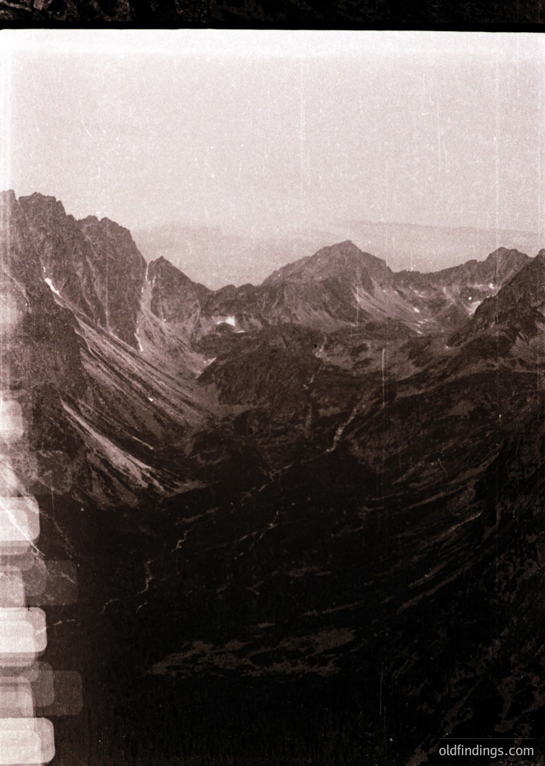 Vintage sepia-toned aerial view of rugged alpine terrain with steep ridges and scattered snow patches. Dramatic rock formations dominate the landscape, likely part of a high-altitude region. Possible early 20th-century photographic technique or reproduction.