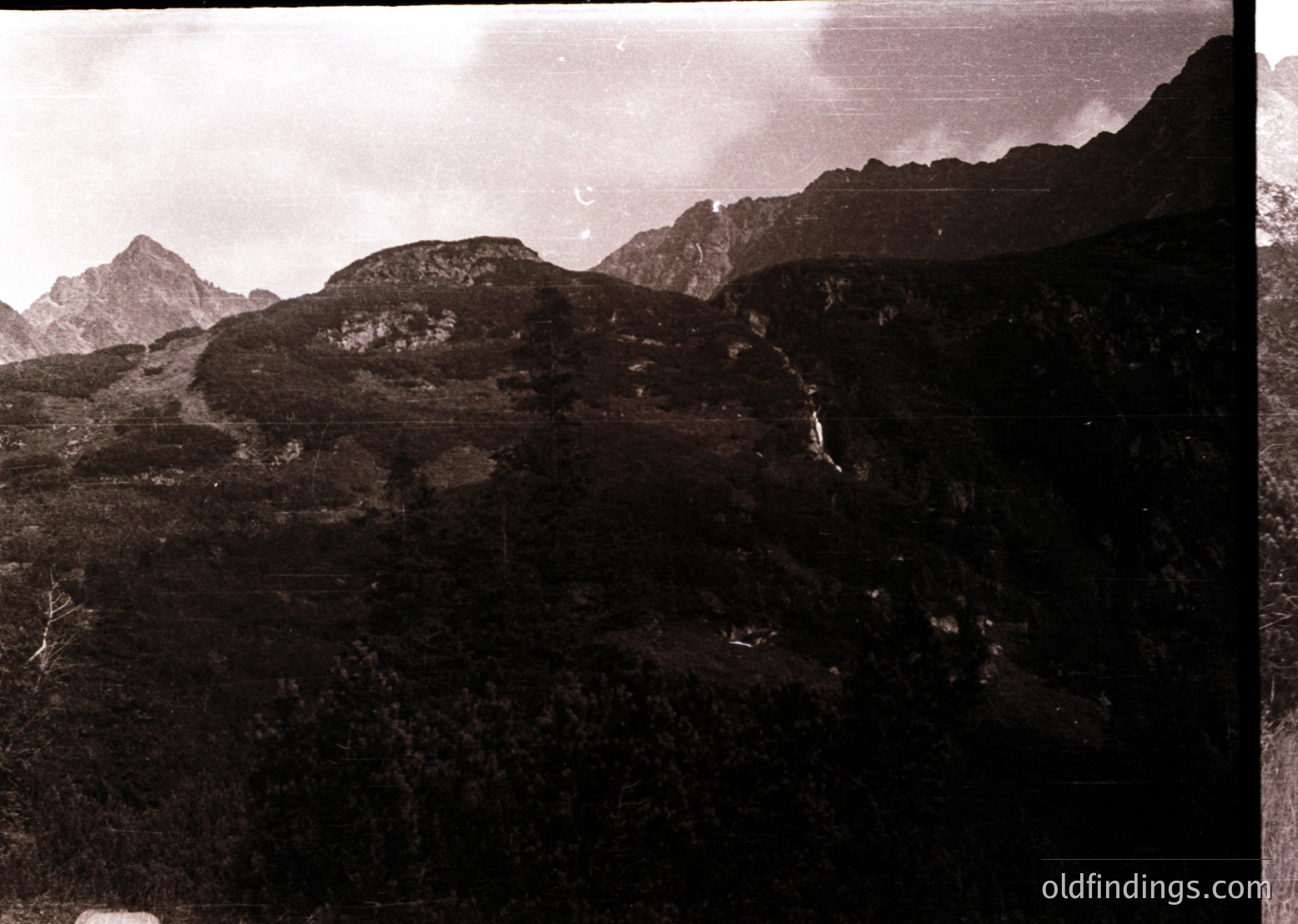 Vintage sepia-toned aerial view of rugged alpine terrain with jagged peaks and sparse vegetation. Distinctive rock formations and a winding waterfall cascade down the slopes. Likely captured mid-20th century for geological or tourism documentation.