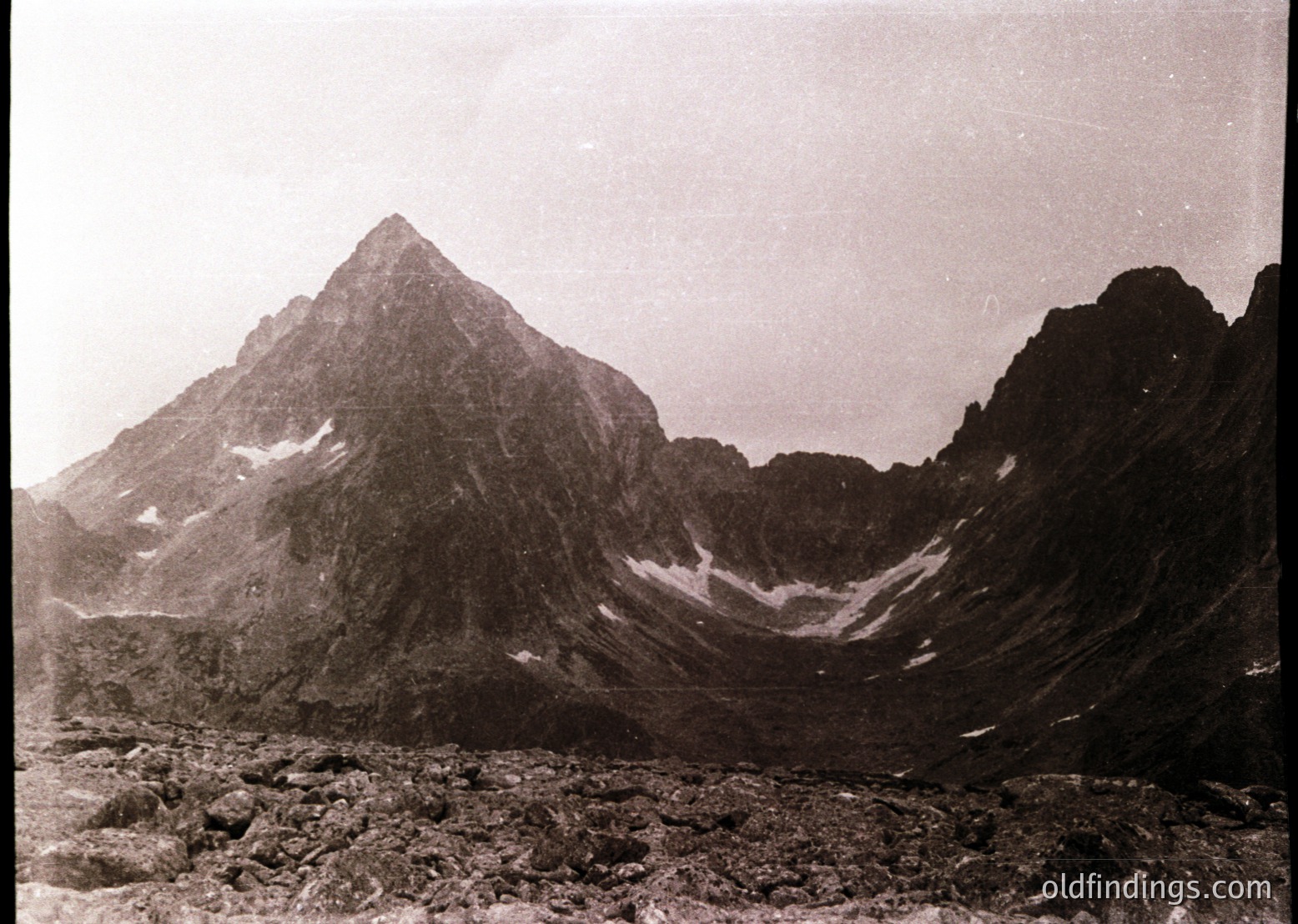 Early 20th-century sepia-toned alpine peak with jagged ridges and snow patches, likely European Alps. Dramatic glacial valley below, rocky foreground.