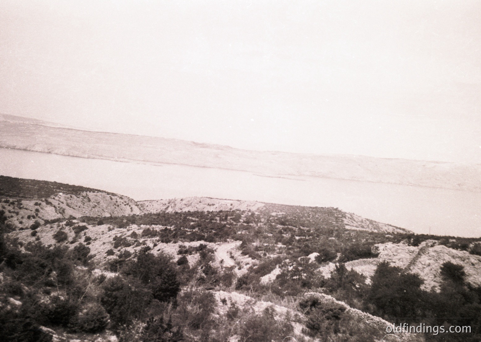 Vintage black-and-white landscape showing rugged, snow-dusted terrain with sparse vegetation. Rolling hills and distant horizon suggest a high-altitude or alpine setting. Likely captured mid-20th century due to photographic style.