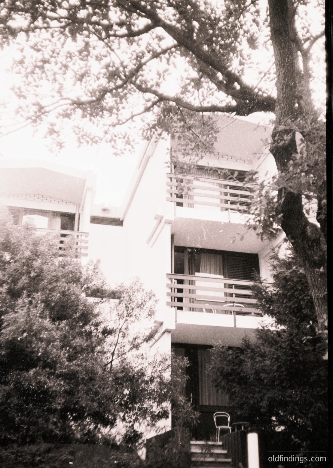 Mid-century modern multi-level building with cantilevered balconies, framed by lush greenery and mature trees. Architectural details include clean lines, concrete structures, and minimalist railings. Likely Eastern European resort architecture, 1960s-1970s.