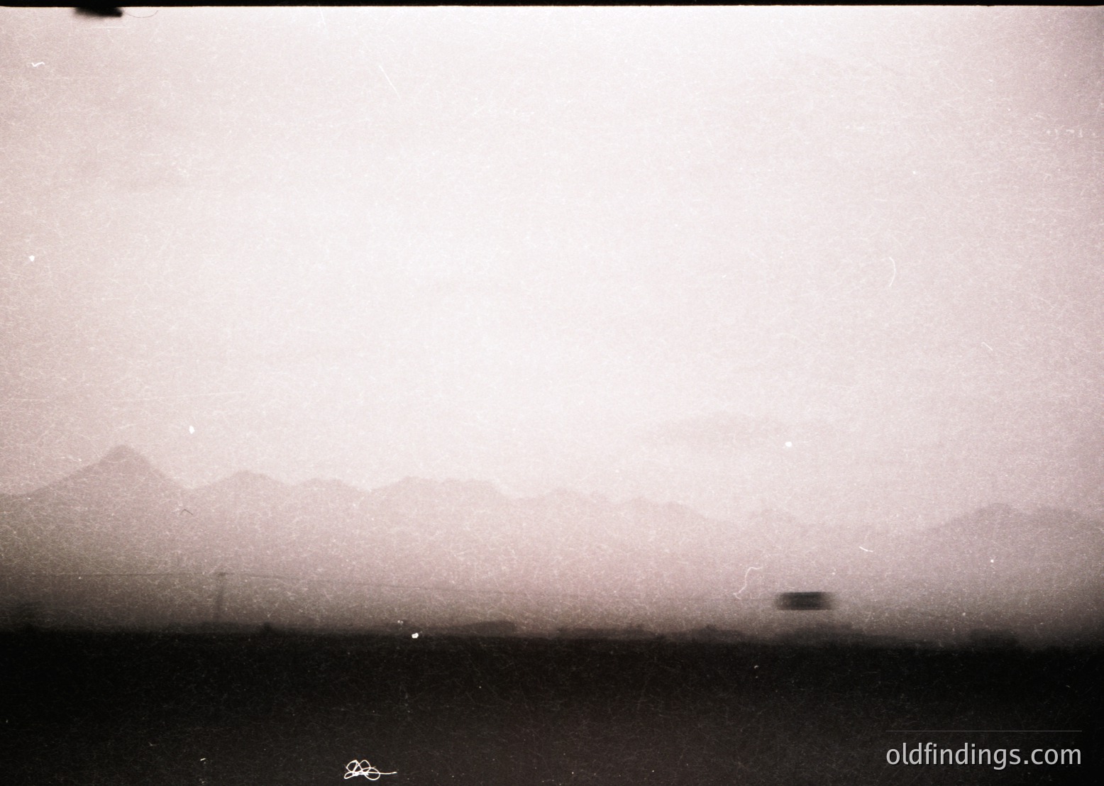 Vintage sepia-toned landscape shot through a window or film grain, revealing faint mountain silhouettes and a distant aircraft. Likely mid-20th century travel or aviation photography.