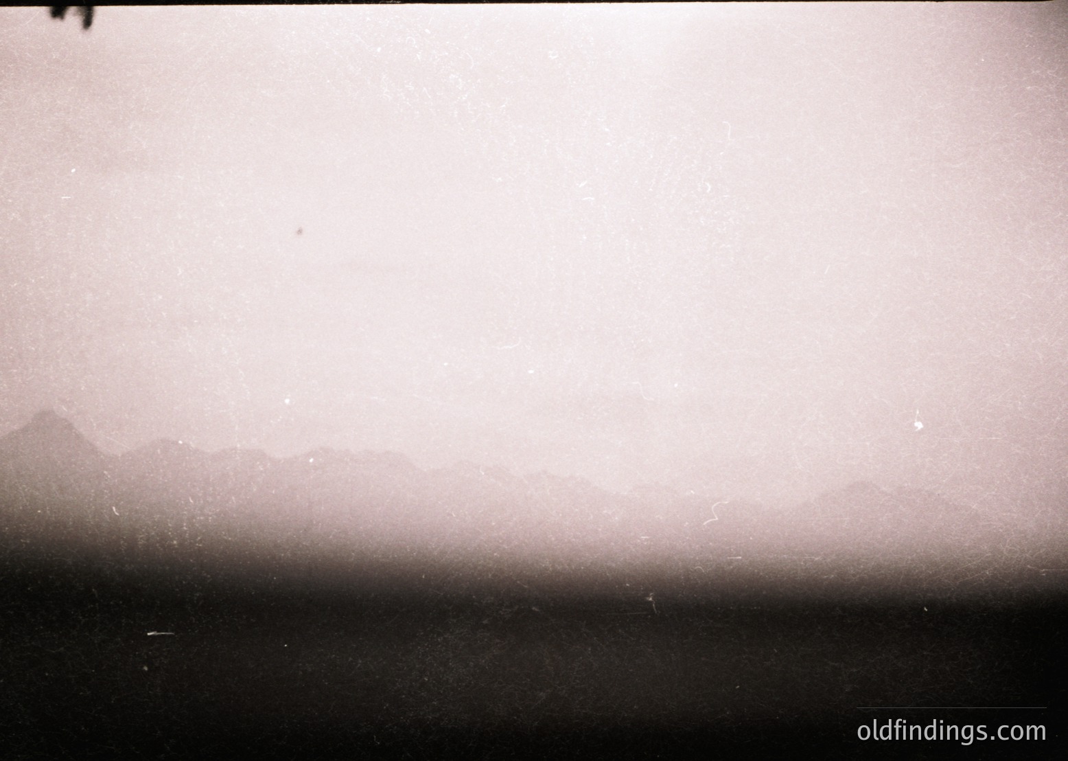 Vintage monochrome shot of a hazy coastal horizon, likely mid-20th century. Silhouetted landforms fade into mist, suggesting fog or low visibility. Composition emphasizes atmospheric texture over detail. Ideal for moody, nostalgic visuals or historical research on early photography techniques.