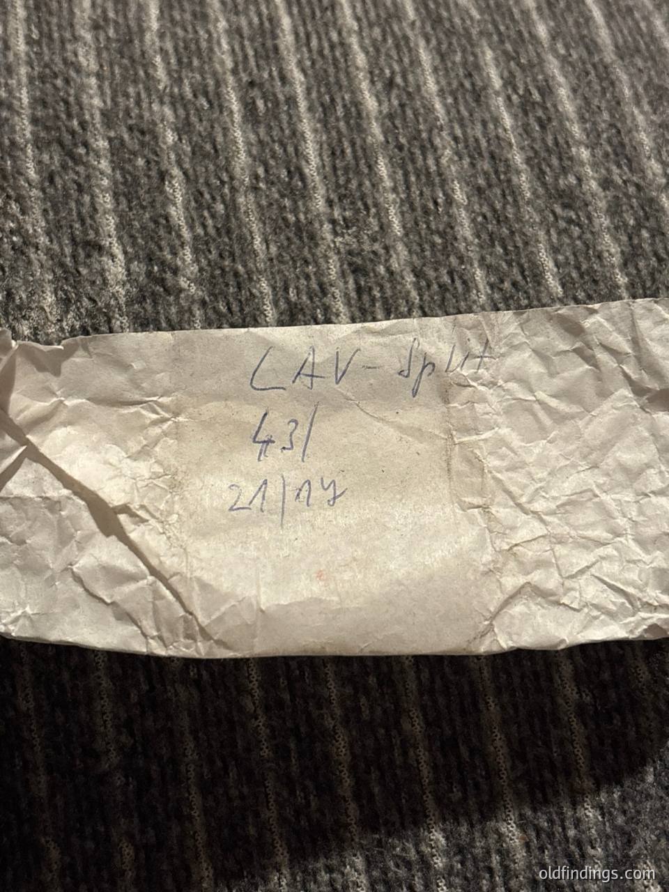 Handwritten label on crumpled paper: "LAV-Split 431 21/07" against dark fabric. Likely a vintage luggage tag or shipping label from Split, Croatia, dated July 21st (year unclear). Useful for travel, archival, or historical research.