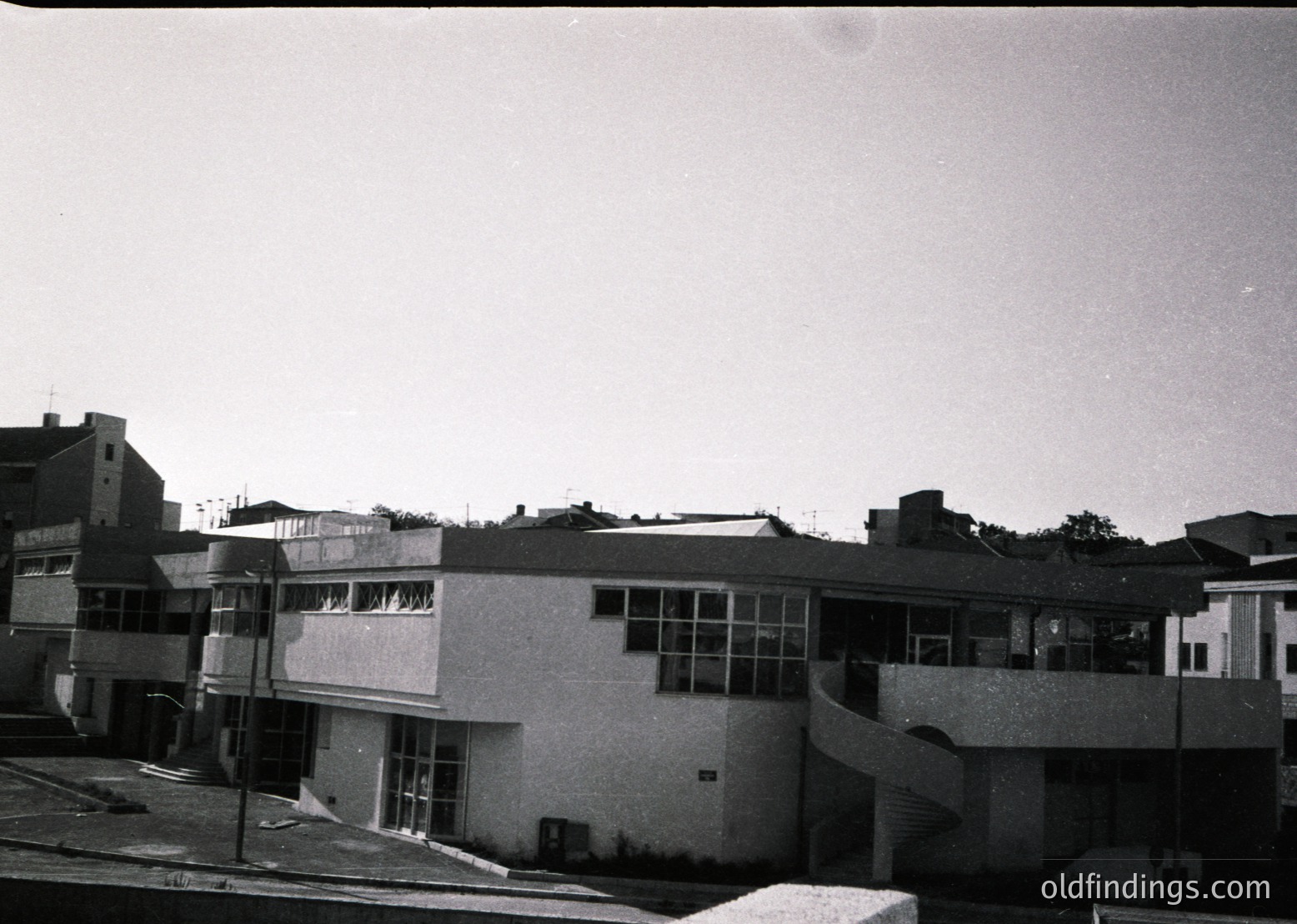 Mid-century Brutalist-style building with raw concrete facade, curved balconies, and large rectangular windows. Urban setting, likely institutional or public use. Black-and-white photo suggests 1960s–1970s timeframe.