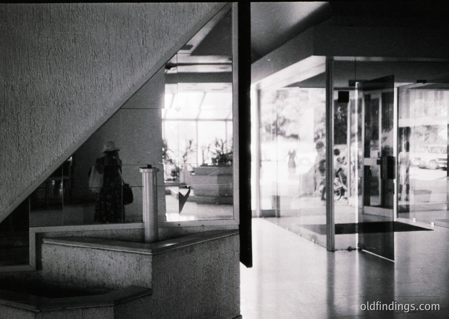 Mid-century Brutalist architecture interior: raw concrete stairwell and reception desk with geometric glass partitions. Reflections reveal blurred figures in a spacious lobby, likely a public or institutional building. Minimalist design with angular lines and functionalist aesthetics.