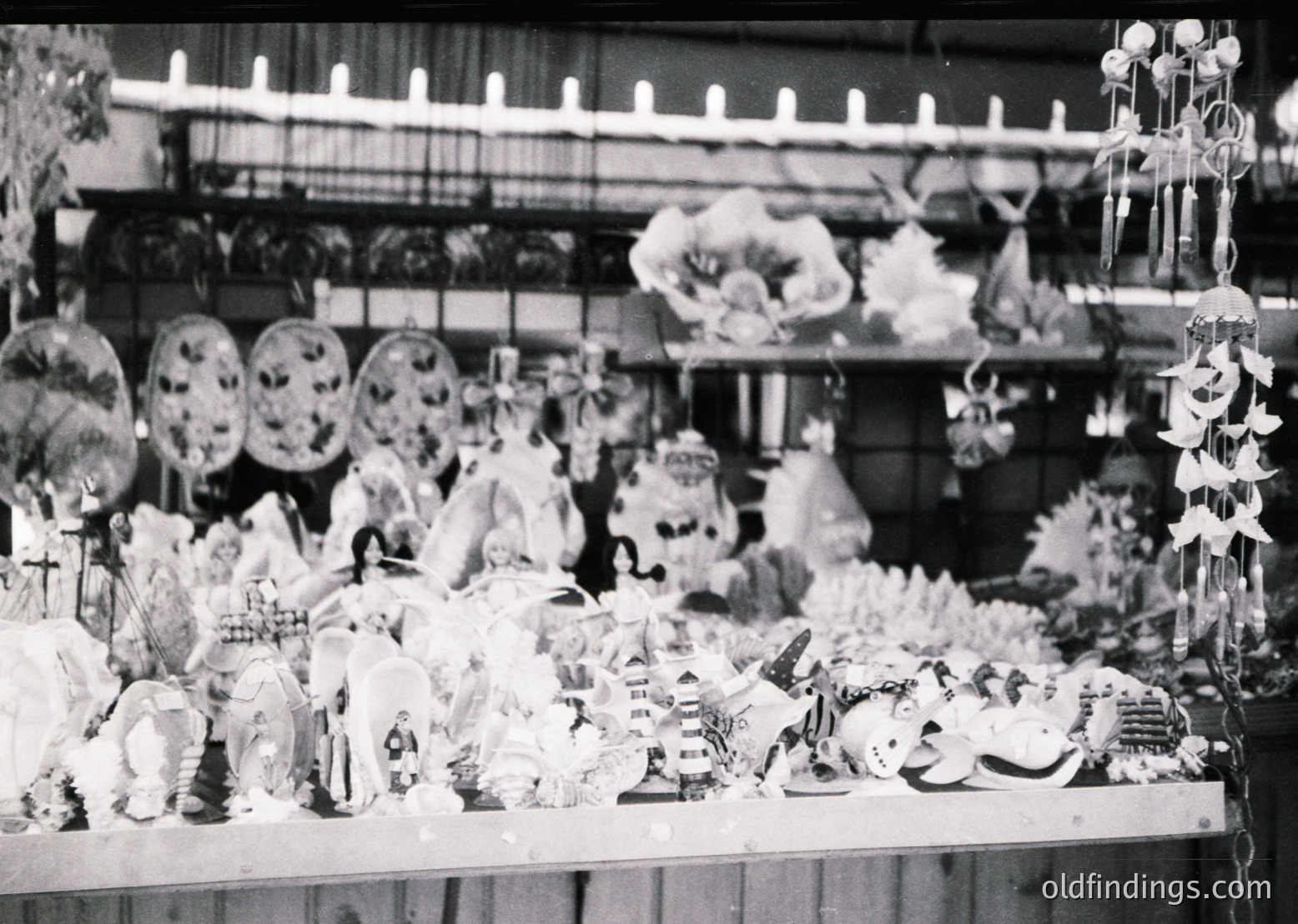 Vintage black-and-white display of ornate holiday decorations—elaborate wreaths, feathered ornaments, and handcrafted figurines arranged on shelves. Likely a 1950s–1960s holiday shop interior, featuring mid-century craftsmanship and seasonal motifs.