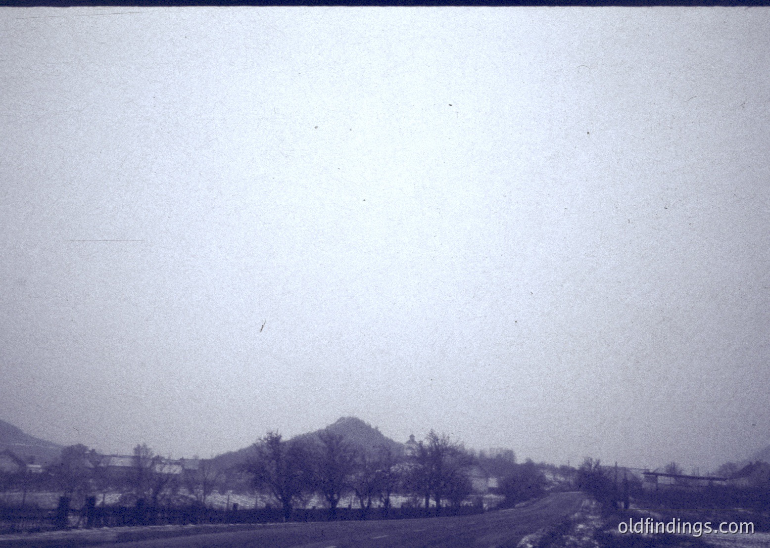Vintage sepia-toned landscape showing a winding rural road flanked by sparse trees and low-lying hills. The muted tones and slight blur suggest early 20th-century photography.
