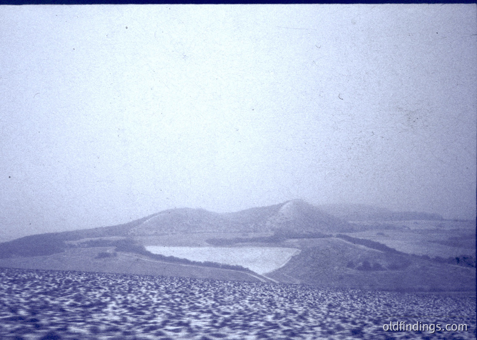 Vintage black-and-white aerial view of terraced hillsides with patchwork agricultural plots. Distinctive stepped farming patterns suggest Mediterranean or Balkan region. Likely mid-20th century due to grainy film texture.