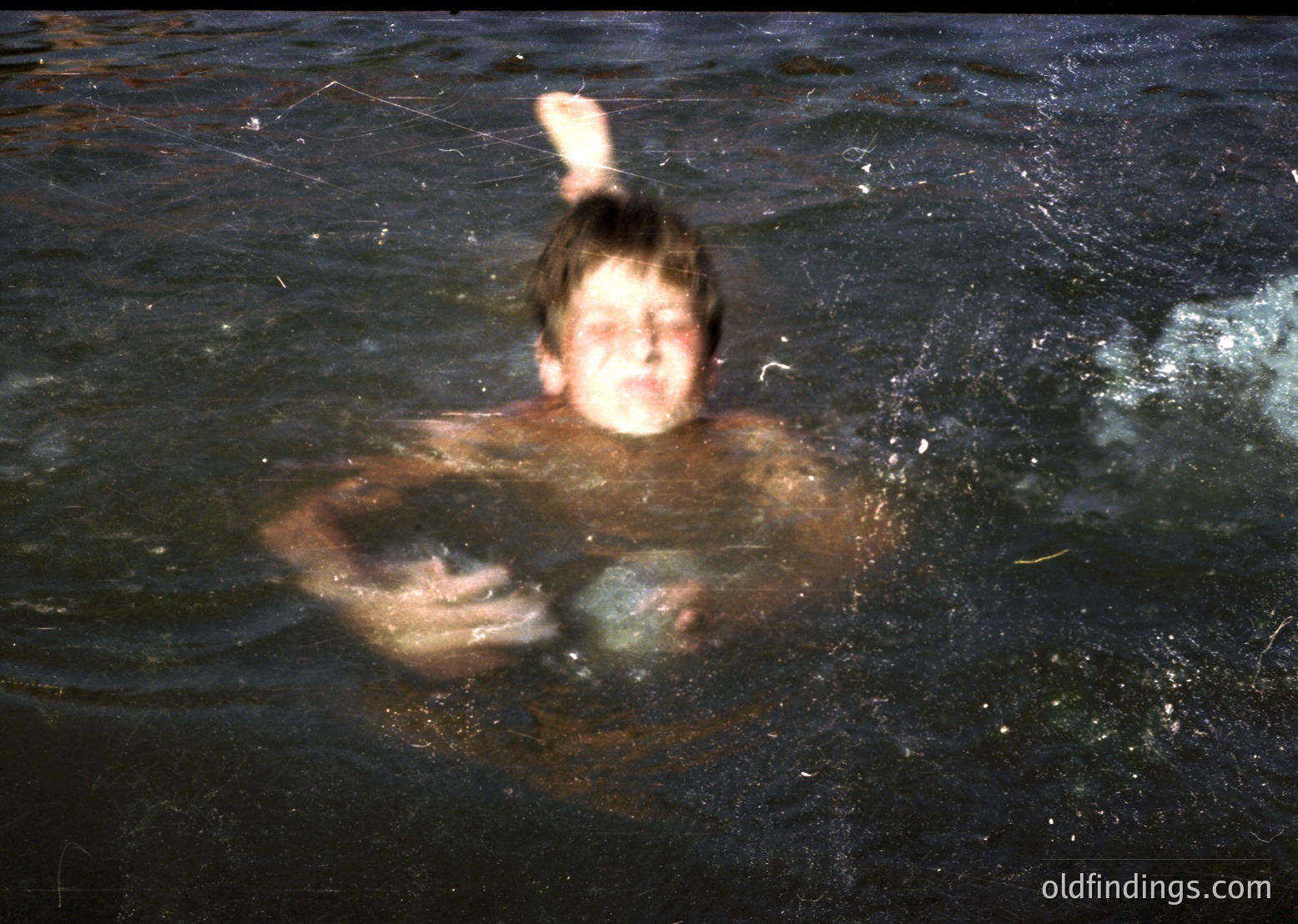 Vintage black-and-white photo of a person submerged in water, holding a spherical object. The dynamic motion blur suggests rapid movement, likely mid-dive or playful splash. Style resembles mid-20th century documentary or candid photography.