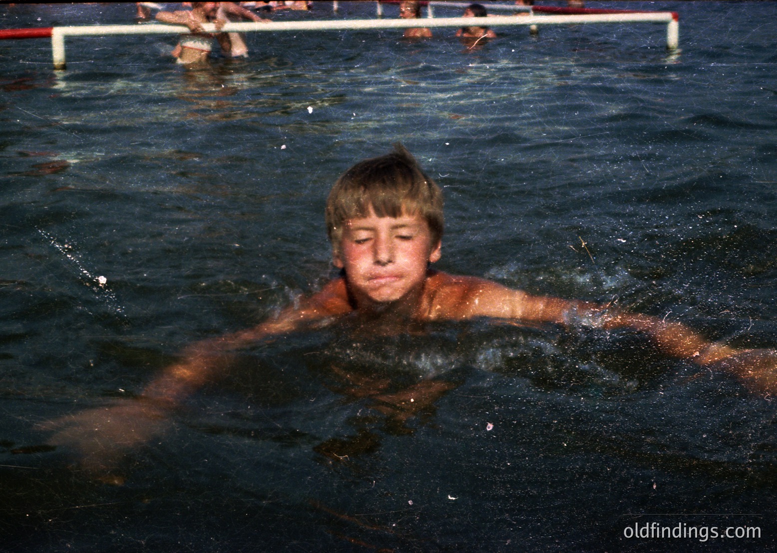 Young boy swimming in a pool, likely mid-1970s–1980s outdoor setting. Note the vintage swim trunks, shallow water, and blurred background indicating motion. Ideal for nostalgic or historical swimming references.