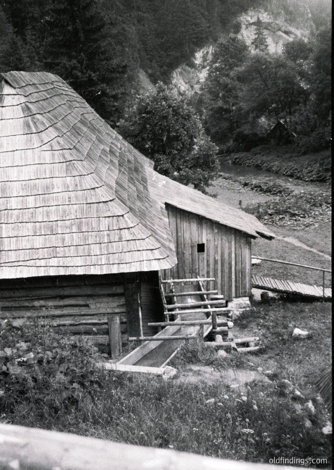 Traditional alpine wooden cabin with shingle roof and wooden plank walls, perched on a forested hillside. Exterior stone steps lead to an elevated entrance. Likely Eastern European alpine region, mid-20th century.
