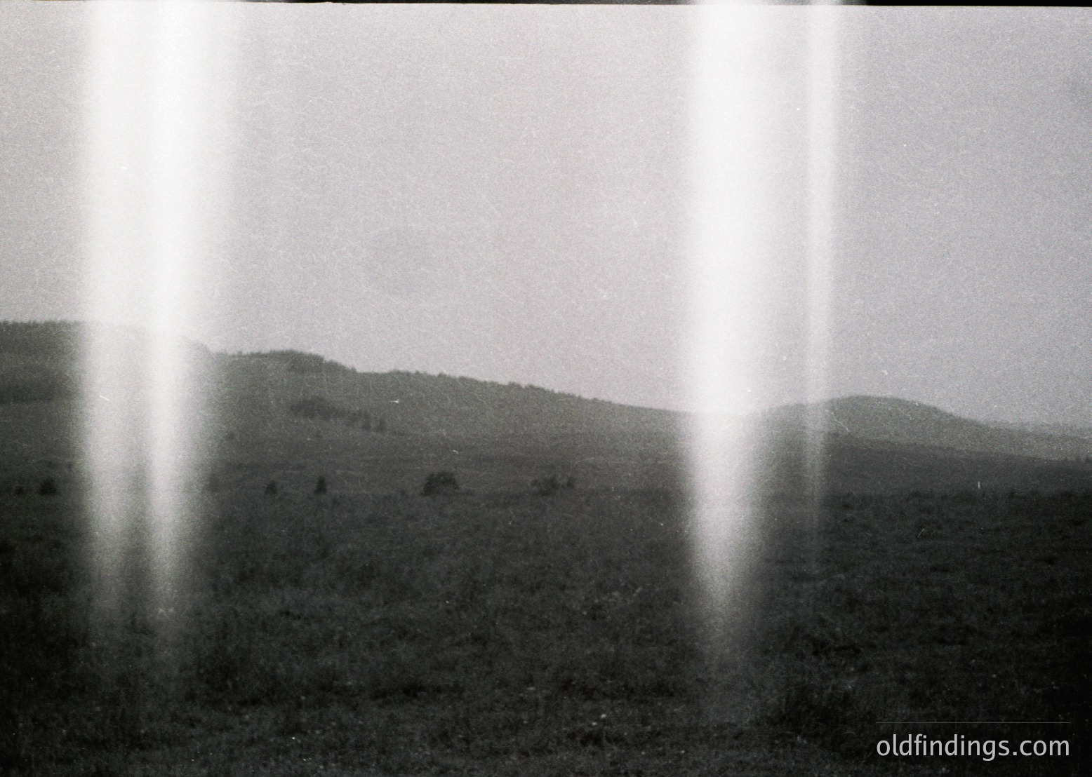 Sunlight streaming through vertical slats creates sharp beams illuminating a misty, rolling landscape. Likely a vintage 35mm film shot, possibly , with a shallow depth of field. The abstract composition evokes and .