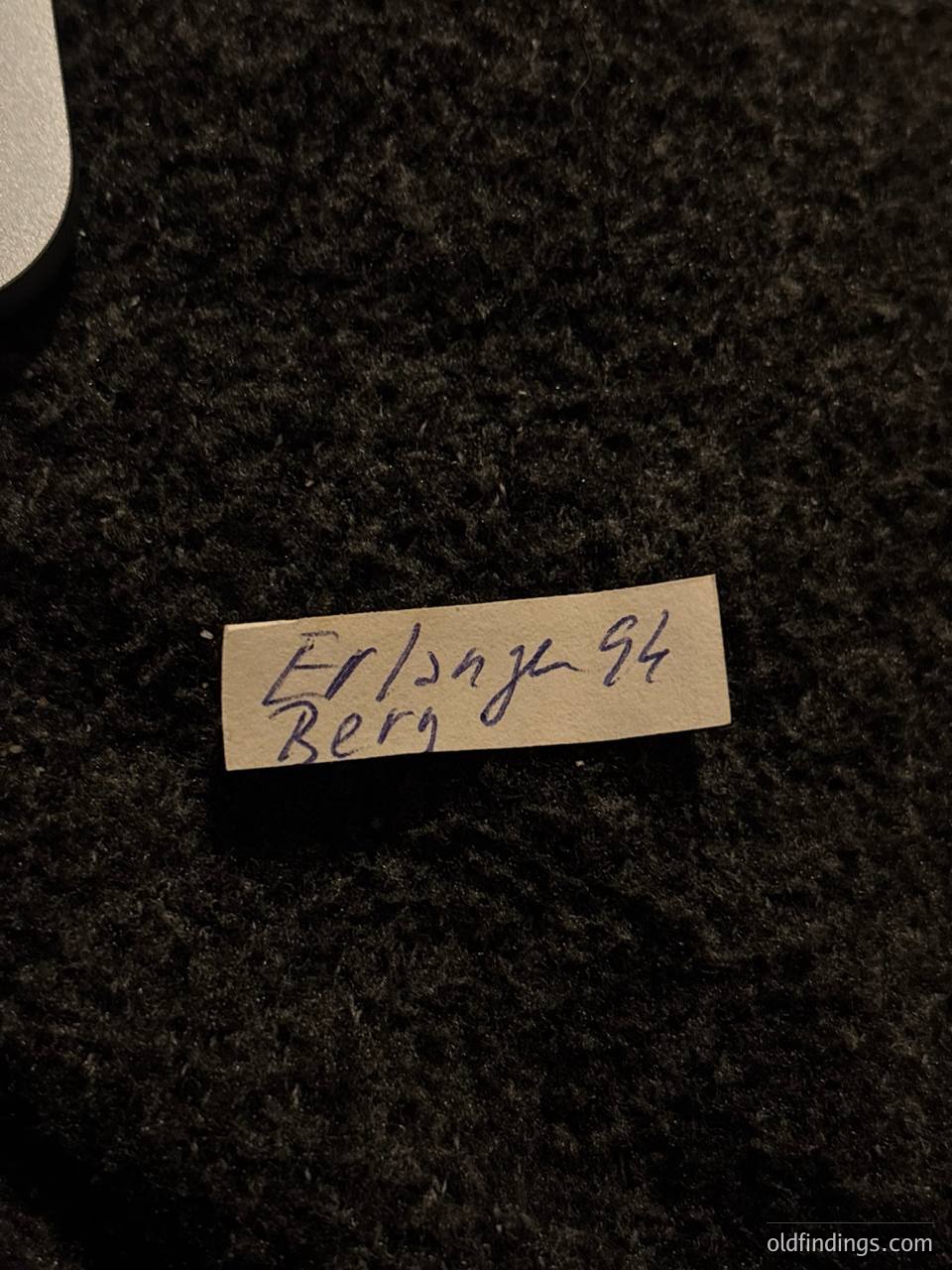 Handwritten label on textured black fabric: "Erlangen '94 Berg." Likely a vintage or archival tag from a 1994 event in Erlangen, Germany.