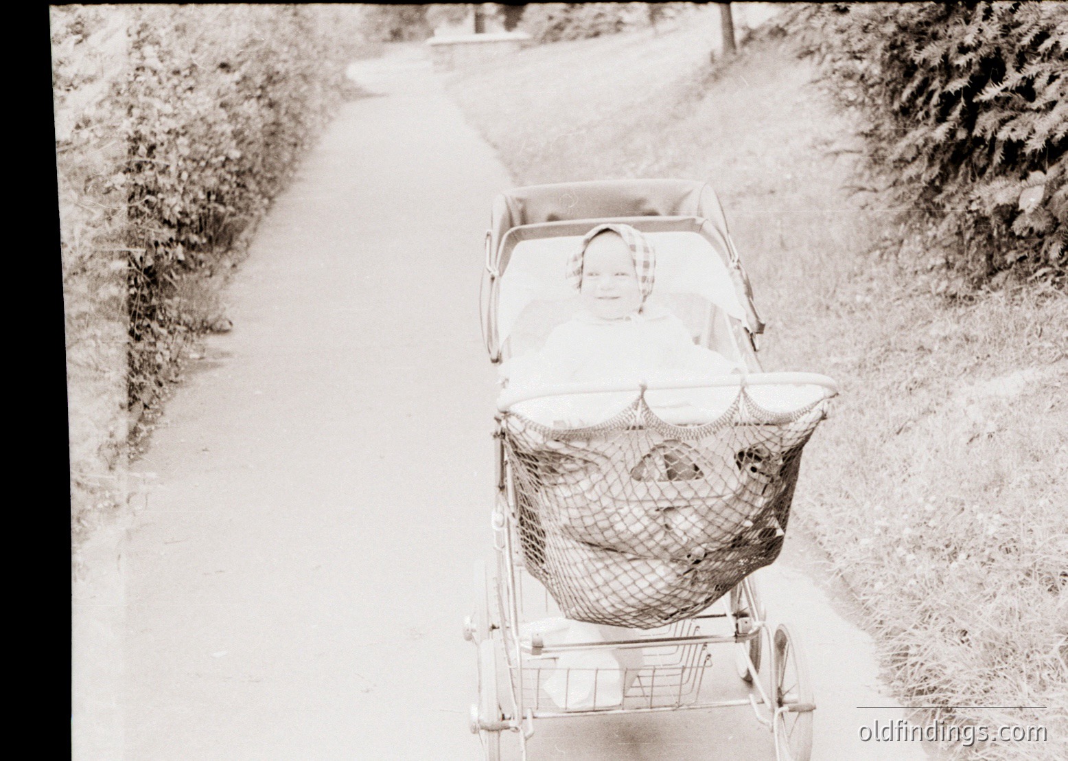 Vintage black-and-white photo of a baby stroller with mesh basket on a rural dirt path, likely mid-20th century. Stroller’s design suggests early post-war European influence.