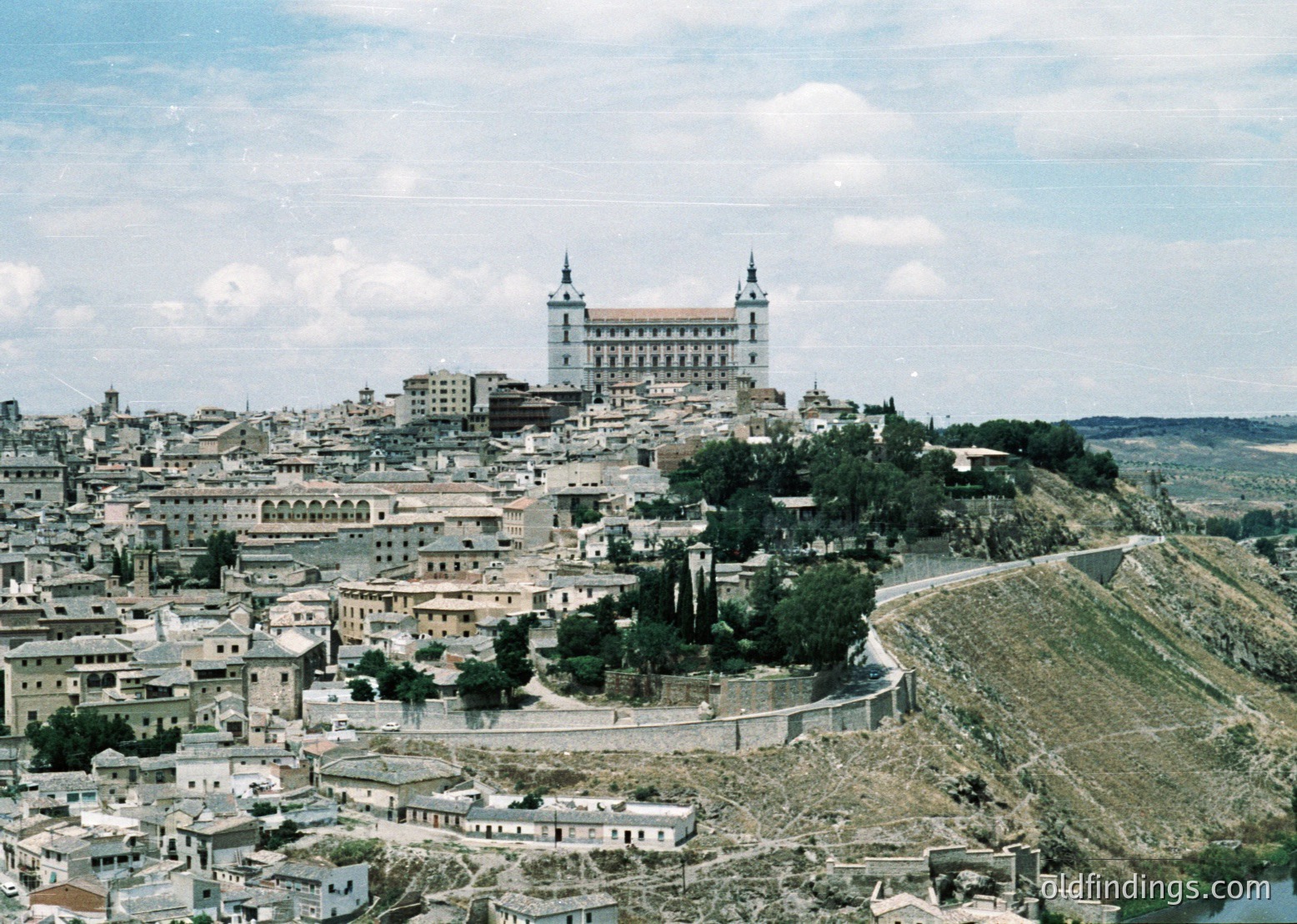 Aerial view of Toledo’s historic skyline, featuring the Alcázar perched atop a hill. Mid-20th century urban layout with clustered whitewashed buildings and winding streets. The Alcázar’s twin towers dominate the horizon, blending into Toledo’s medieval architecture.