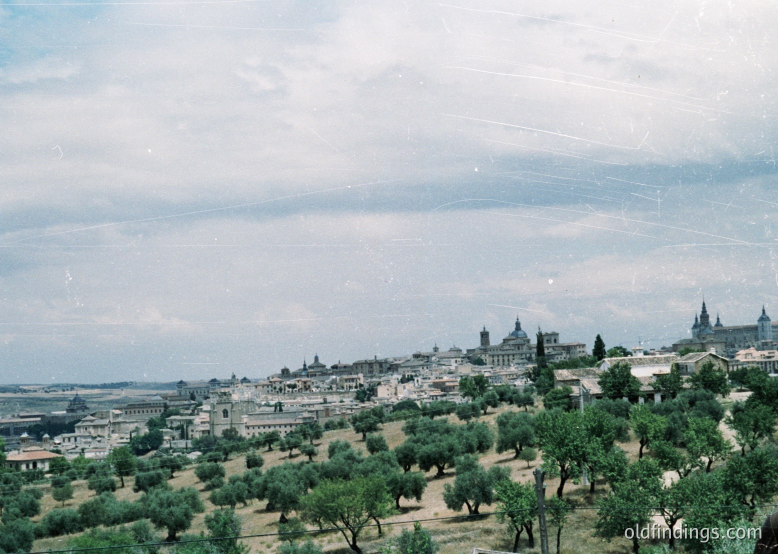 Vintage aerial view of Madrid’s skyline with lush olive groves in foreground. Distinctive domes of the Royal Palace and surrounding historic architecture visible. Mid-20th century urban landscape with classic Spanish architectural styles.