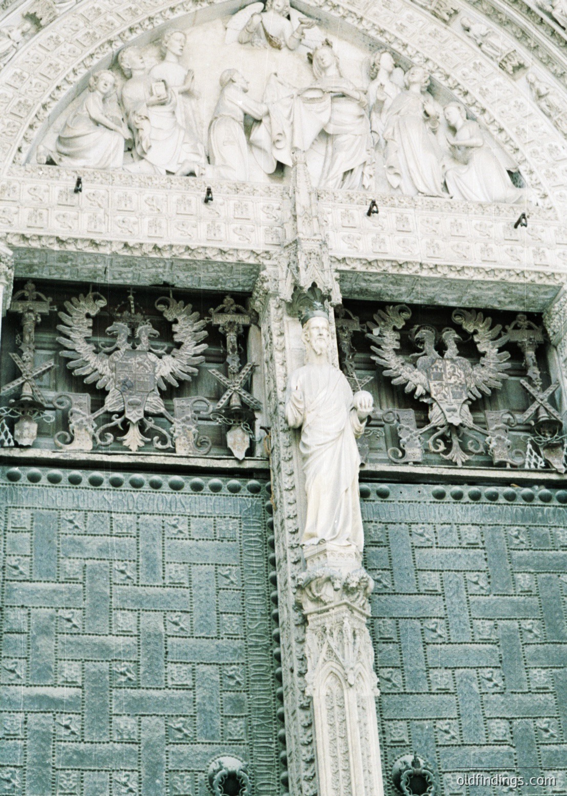 Neoclassical stone facade featuring intricate relief sculptures. Central figure in draped robes holds a scroll, flanked by double-headed eagles with spread wings. Above, a frieze depicts classical figures in dynamic poses. Architectural style suggests 19th-century European influence, likely public or institutional building.