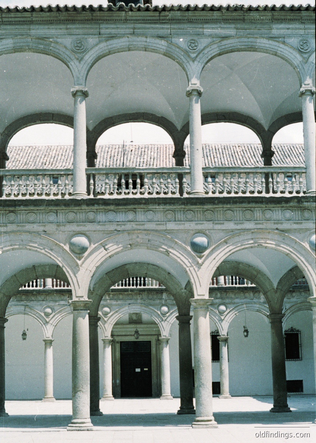 Renoir-style courtyard with double-tiered arcades featuring classical columns, balustrades, and spherical finials. Stonework showcases intricate carvings and rounded arches. Likely European, 16th–17th century.