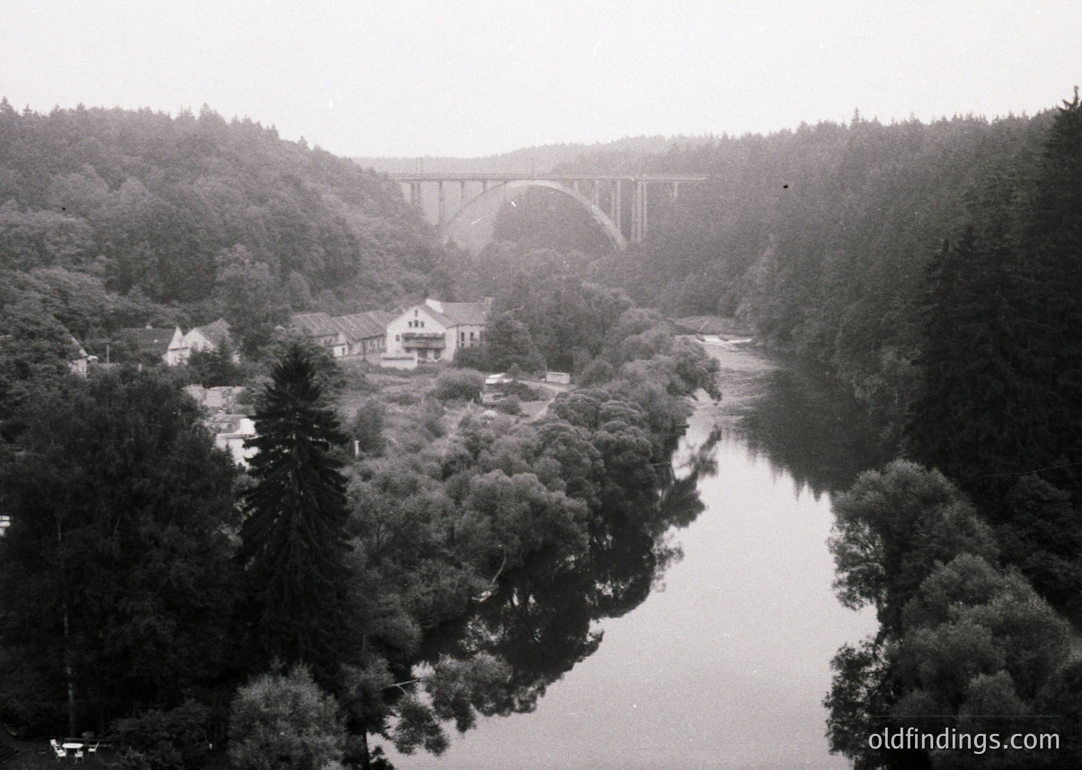 Vintage black-and-white aerial view of a grand arched viaduct spanning a river, flanked by dense forest. Mid-20th century industrial architecture contrasts with natural surroundings, likely a European railway landmark.