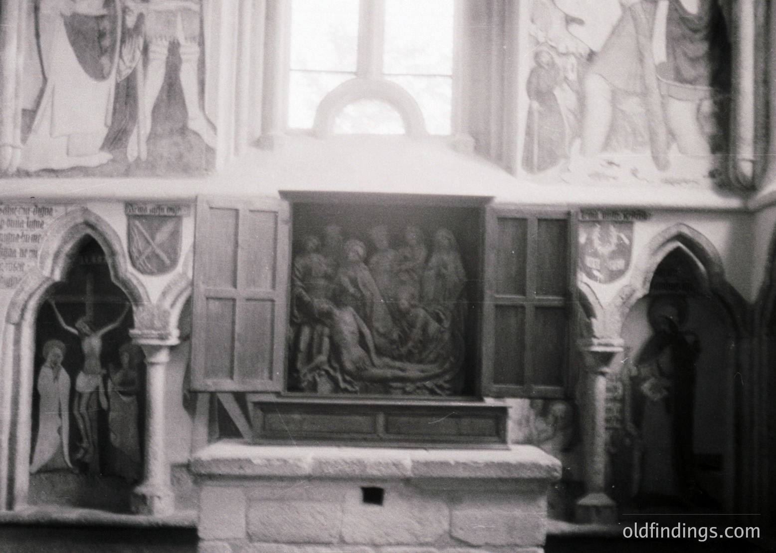 Relief sculpture of Christ’s entombment flanked by Gothic-style altarpiece panels depicting crucifixion and resurrection scenes. Stone carvings and frescoes suggest medieval ecclesiastical architecture, likely 13th–15th century.