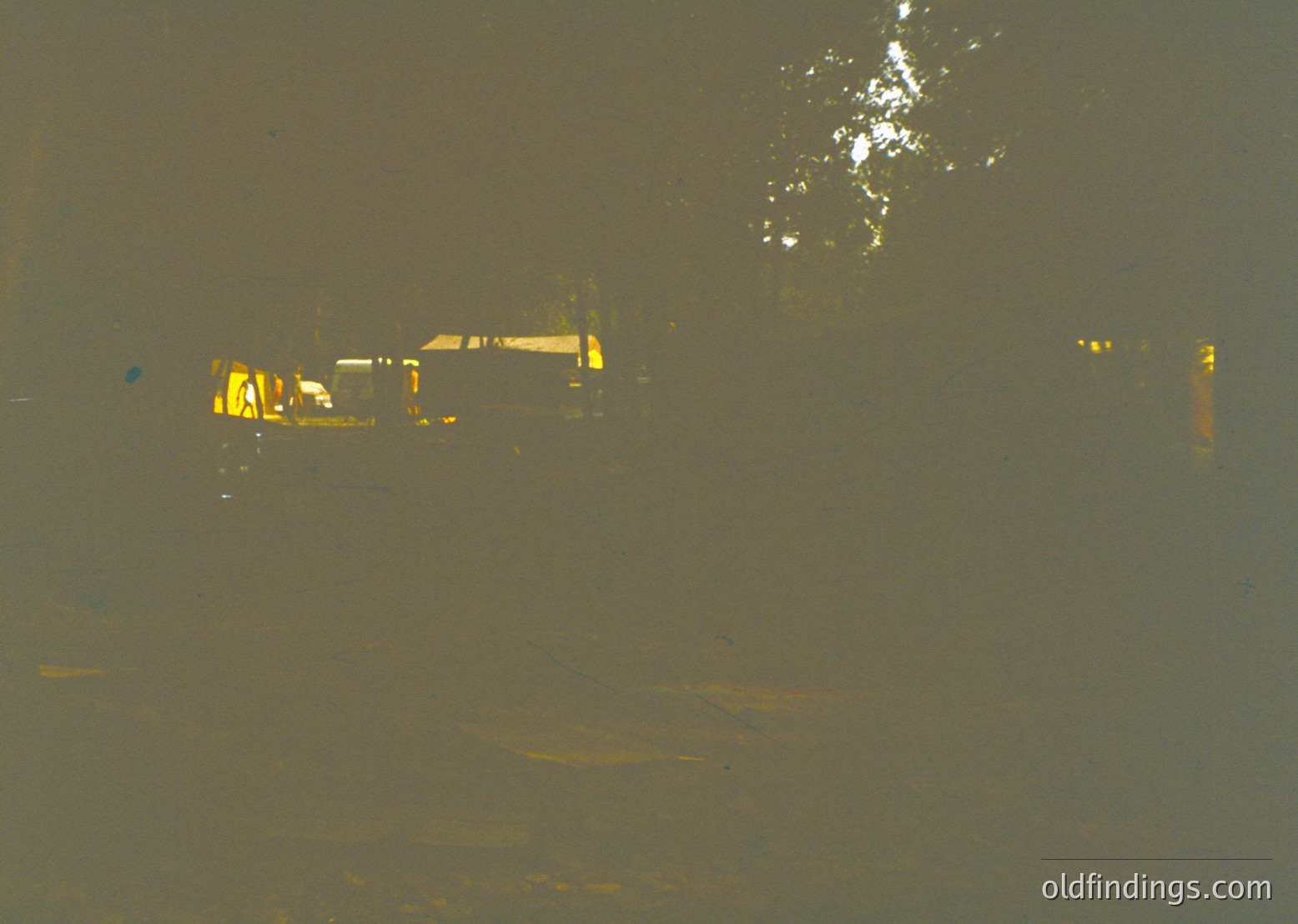 Vintage sepia-toned photo of a dimly lit industrial scene, featuring a single-story brick building with yellow-painted windows and doors. Yellow caution markings on pavement suggest restricted access. Overcast sky and muted lighting evoke early-to-mid 20th-century factory or warehouse setting.