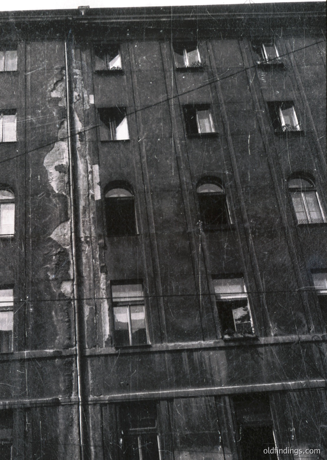 Mid-century urban architecture featuring a multi-story brick facade with arched window frames. Visible wear and exposed wiring suggests aging infrastructure. Likely Eastern European -70s construction.