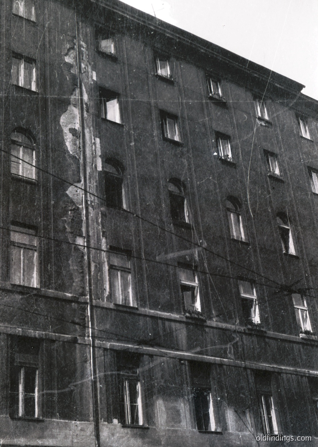 Mid-century Soviet-era apartment block under renovation, featuring scaffolding and exposed brickwork. Symmetrical windows with arched tops and concrete framing reflect urban Soviet architecture. Likely Eastern Bloc, 1960s–1980s.