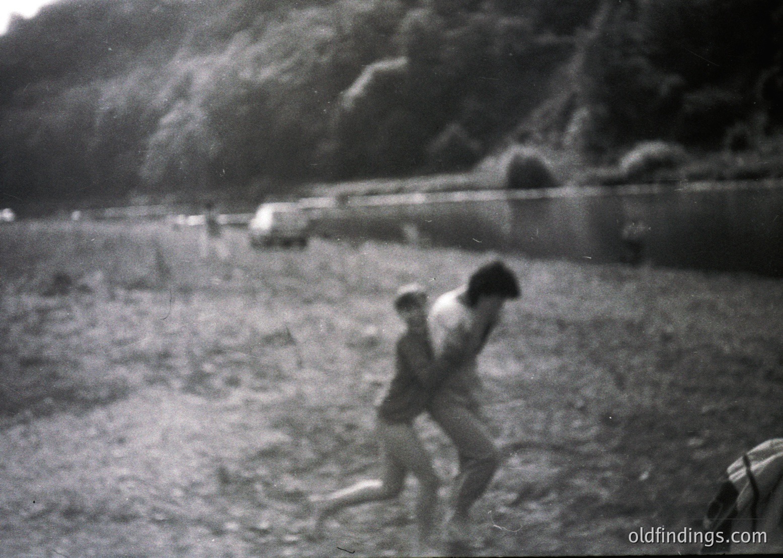 Mid-20th century black-and-white photo of two children playing near a rocky hillside. Blurred motion captures dynamic energy. Vintage clothing suggests or . Rural or semi-rural setting with minimal structures visible. Ideal for historical or nostalgic stock imagery.