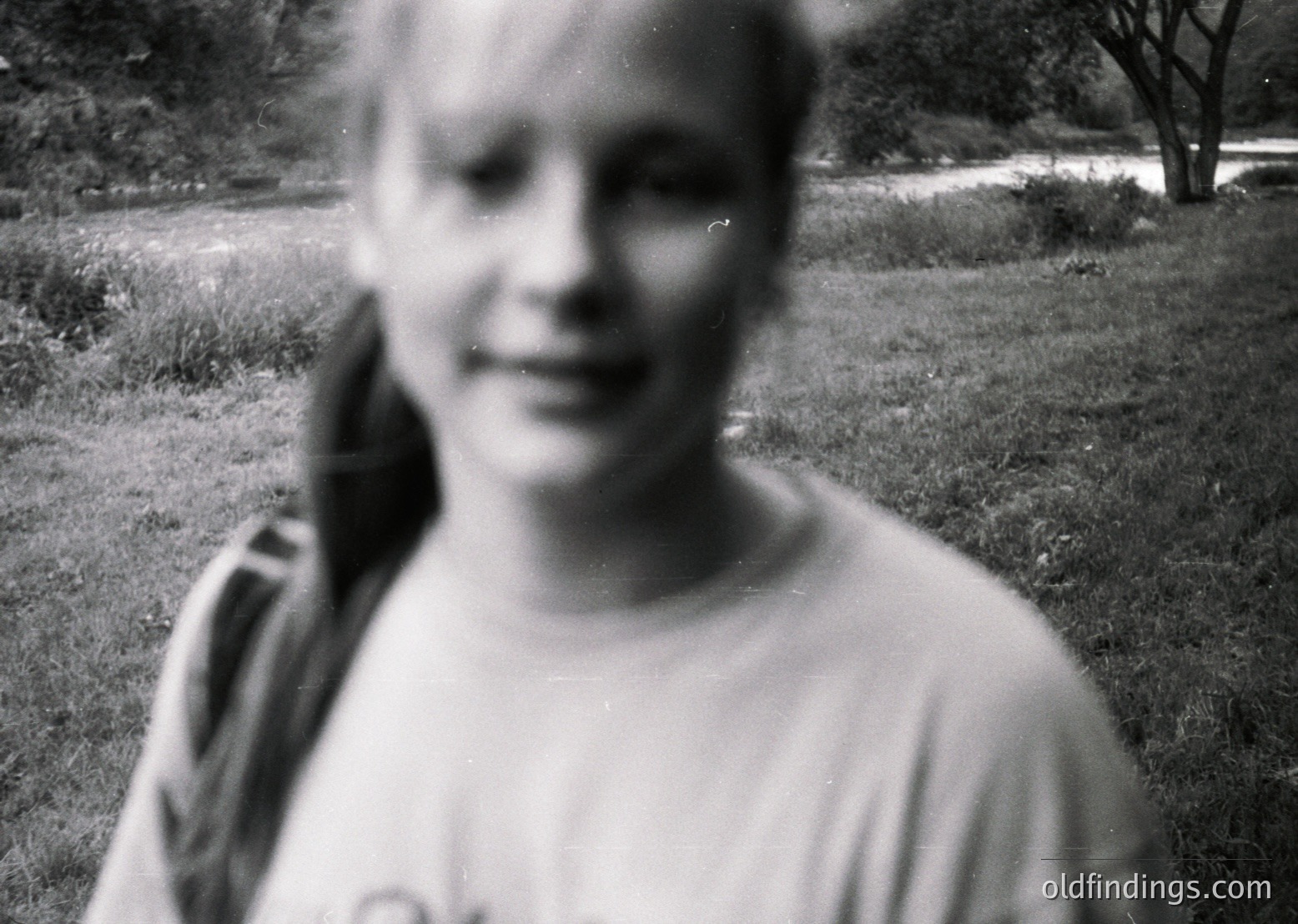 Vintage black-and-white portrait of a young person outdoors, blurred for privacy. Light-colored short-sleeve shirt with indistinct print. Soft focus suggests candid, mid-20th-century style. Ideal for nostalgic or historical research.