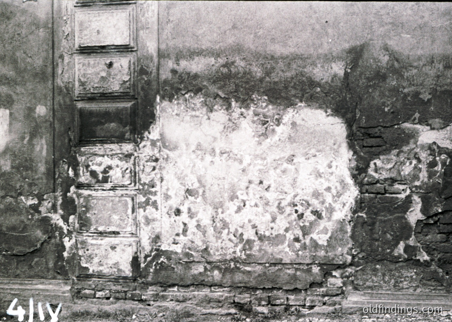 War-damaged building facade with exposed brickwork and plaster collapse, likely post-WWII. Distinctive vertical stone columns remain intact.