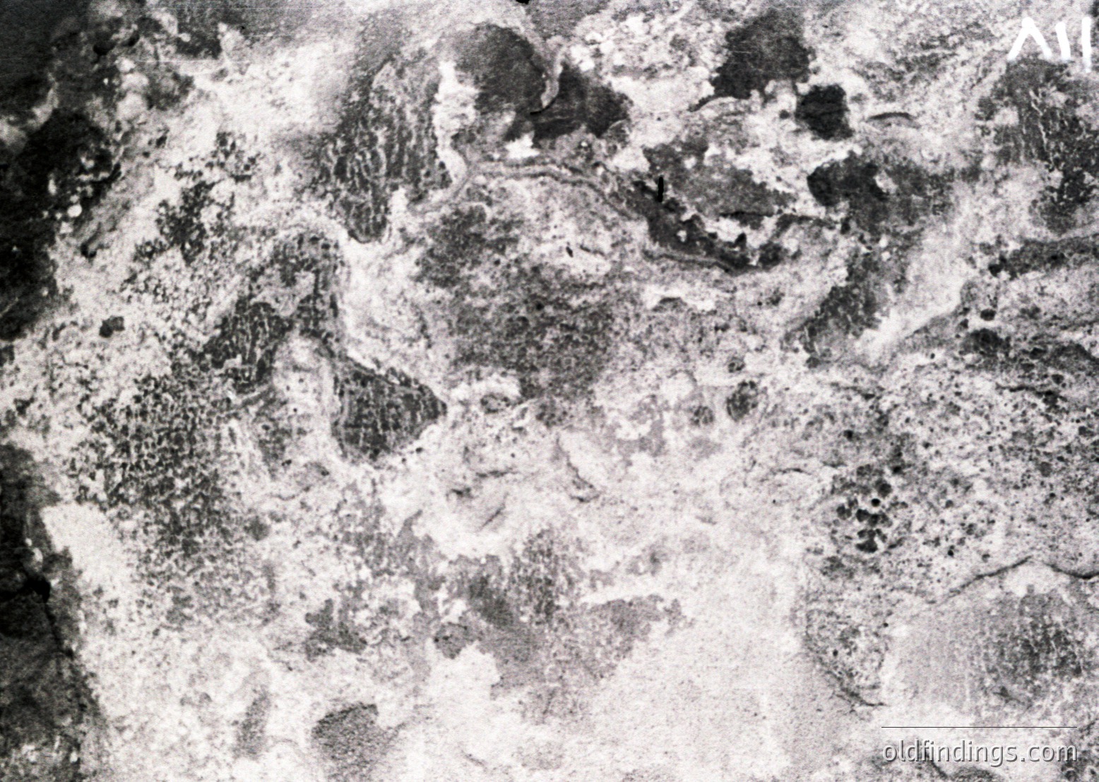 High-contrast aerial photo of bombed terrain, likely WWII-era. Dense craters and debris suggest heavy artillery or bombing damage. Texture resembles lunar-like impact zones.