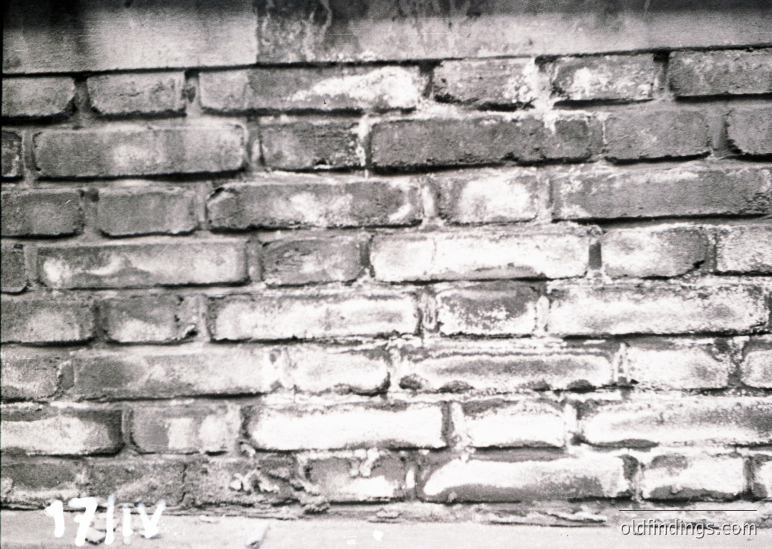 Close-up of weathered brick wall with visible mortar erosion, likely mid-20th century industrial or residential architecture. Darkened mortar joints and cracked plaster reveal structural aging.