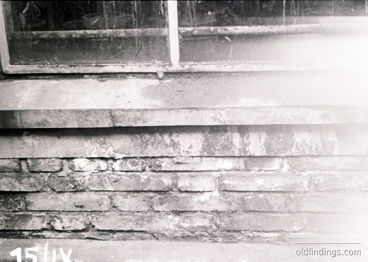 Close-up of weathered brick facade with cracked plaster and exposed mortar, likely from early-to-mid 20th century architecture. Visible window frame and ledge suggest residential or institutional use.