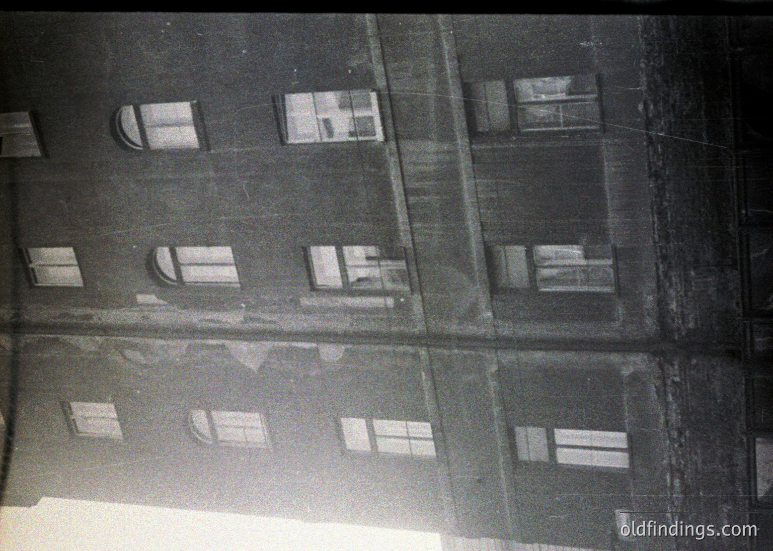 Mid-century Soviet-era apartment block façade with uniform concrete panels, arched windows, and visible wear. Likely Eastern Bloc architecture, 1960s–1980s.