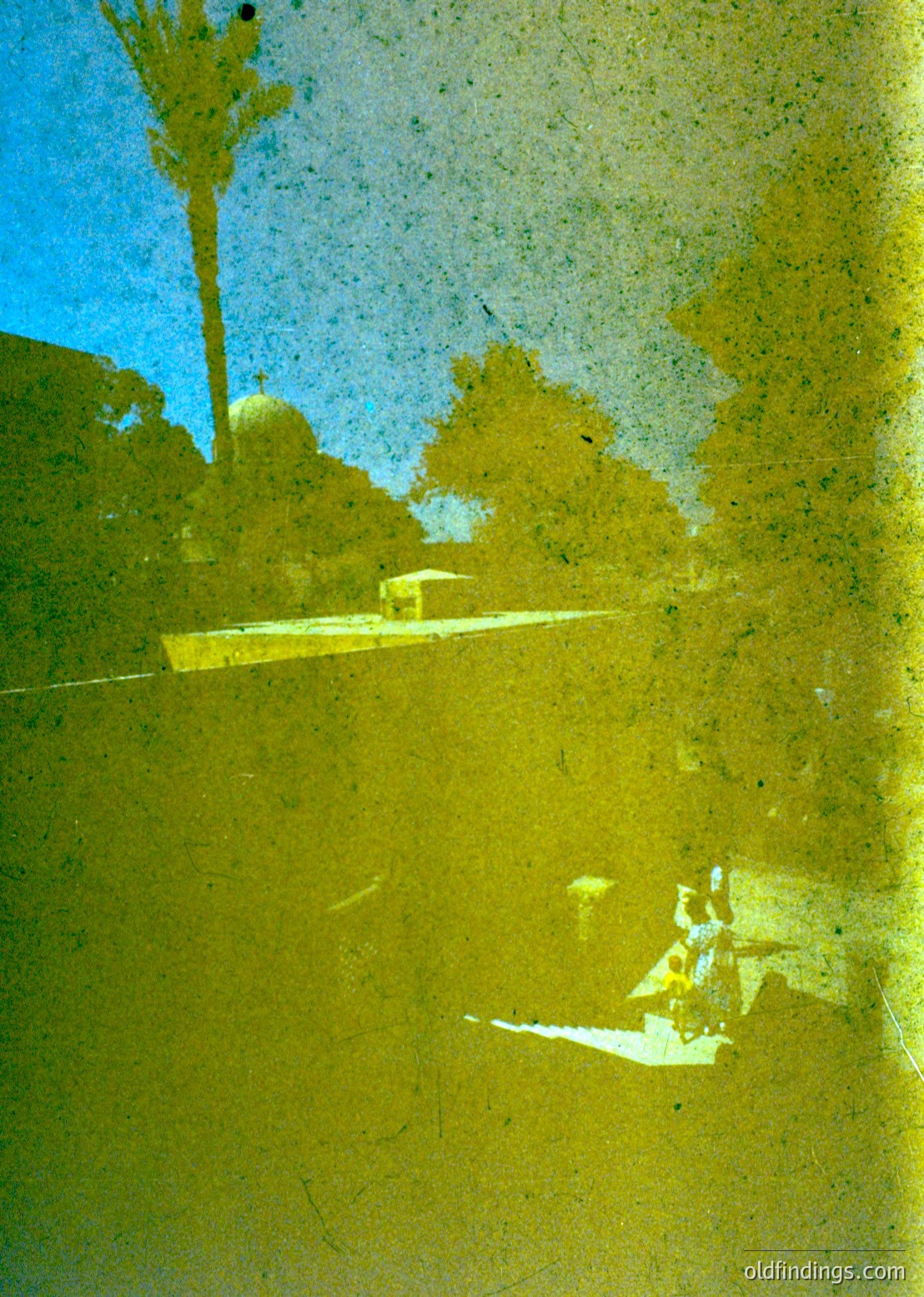 Vintage aerial reflection on aged glass, showing a rural landscape with a single-story building and scattered trees. Distorted but recognizable as a farm or countryside scene, likely mid-20th century. Yellowed tint suggests archival or historical photography.