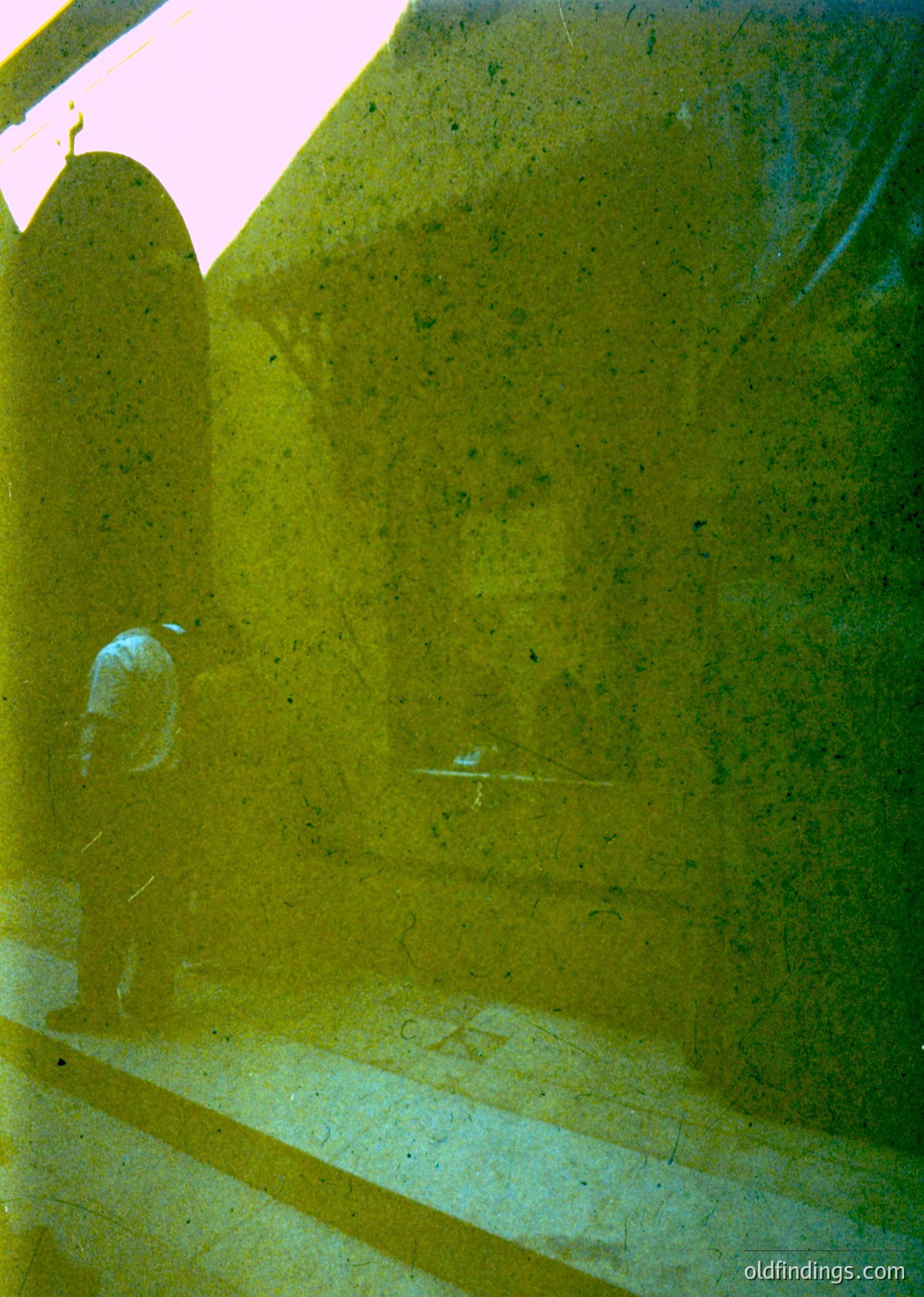 Reflection of a lone figure in a yellow-tinted glass wall, likely a modern office or institutional building. The person appears to be walking with a cane. The text "CO" and "21" are visible on the floor. The composition suggests a minimalist, contemporary architectural style.