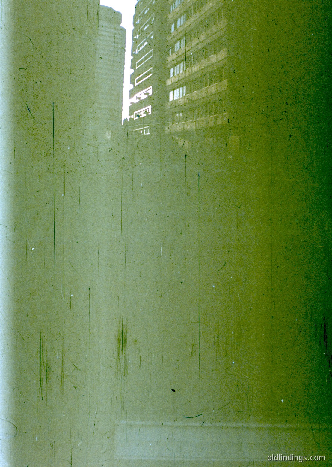Reflection of high-rise buildings through a slightly fogged or scratched glass pane, likely a window. Urban architecture with horizontal window bands and vertical columns visible. Potential mid-20th century cityscape, possibly European.
